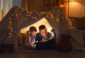 happy family father and children reading a book in tent at home