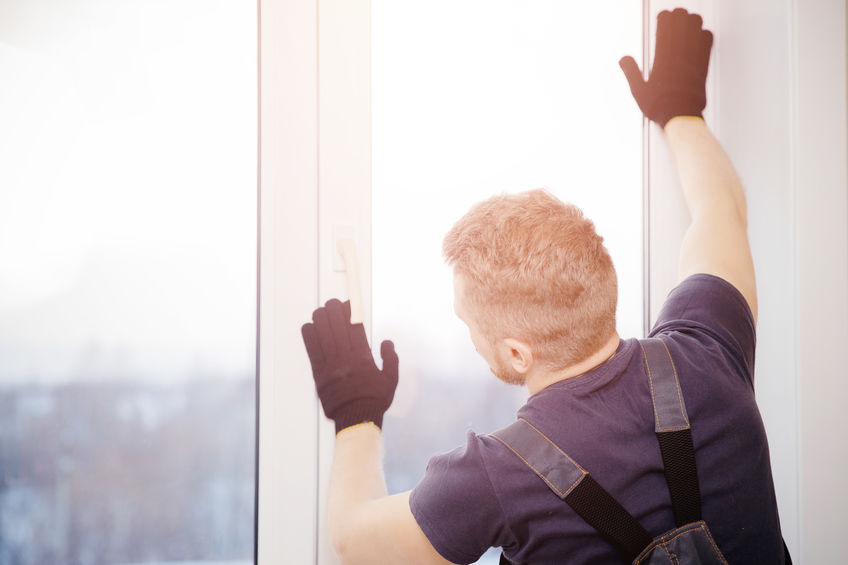 Male builder installs and checks plastic windows in apartment ho