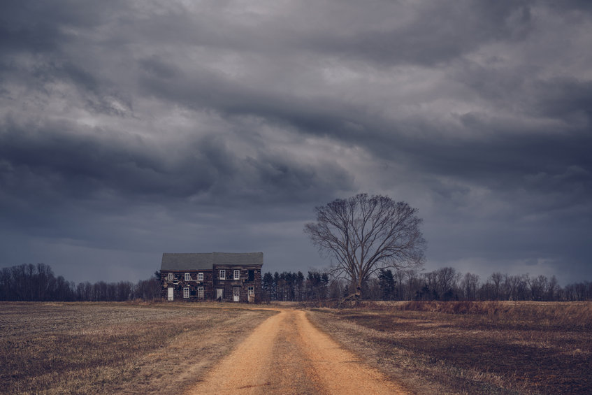 Dirt road leading to a haunted house with dark rain clouds